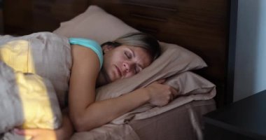 Bright sunlight wakes up young woman in bed. Positive morning awakening concept