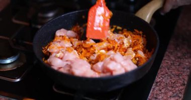 Cook or housewife fries chicken fillet meat with carrots in frying pan. Cooking meat concept