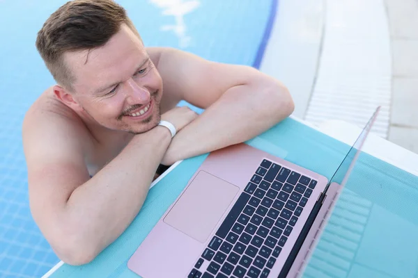 Young handsome man in pool with laptop. Remote work freelancer works anywhere in world