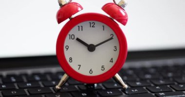 Red alarm clock on a black laptop keyboard, close-up. Deadline concept, efficiency increase, work