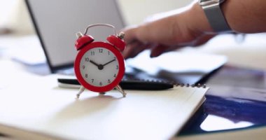 Red alarm clock on the table in the office near the laptop, shallow focus, close-up. Workspace of an office work