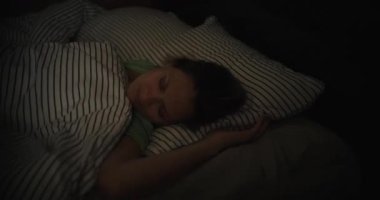 Genç bir kadın fırtına sırasında yakın planda evinde uyuyor. Pencerenin dışındaki şimşek ışığı