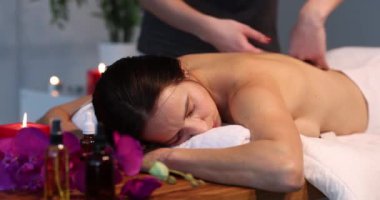 Bir masör onu sırtüstü uzanan güzel bir kadına doğru okşar, yakın plan. Güzellik salonunda spa tedavisi