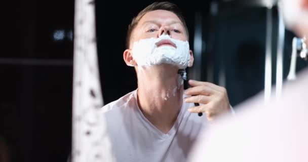 鏡の前の若い男がかみそりのクローズアップで髭を剃っている 刺激のないシェービング メンズ化粧品 — ストック動画