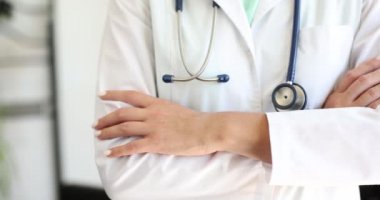 Doktorun kolları göğsünde, muayenehanede bağlı duruyor. Güvenilir doktor ve sağlık sigortası ve yardım
