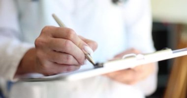 Doktor kadın elinde kalem kağıdıyla panoya yakın çekim yapıyor. Hasta ve sağlık sigortası hesaplamalarını kontrol etmek için koğuşta dolaşıyorum.