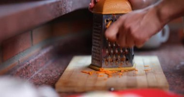 Dişi eller taze havuçları rendeleyiciye yakın çekimde ovalarlar. Sebze pişirme ve faydaları