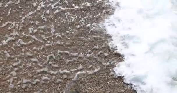 スローモーションビデオ白い泡の波は 晴れた日の概念上の海辺の小石暗い石で岸に洗浄されます — ストック動画