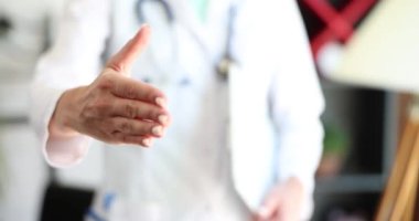 Tıp doktoru klinikte yakın çekimde el sıkışmayı teklif ediyor. Selamlar ve hoş geldin jestleri ve doktorun el sıkışması.