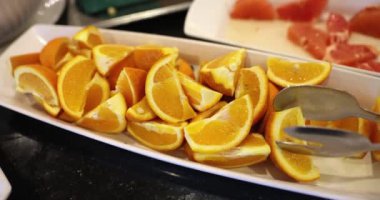 Uzun, dikdörtgen beyaz bir tabakta dilimlenmiş sarı limonlar, yakın plan. Oteldeki siyah bir masanın üzerinde turunçgil meyveleri, kahvaltı.