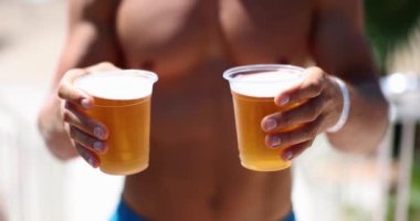 Plajda çıplak gövdeli atletik bir adam plastik bardakta soda tutuyor, yakın plan. Yaz tatili kavramı