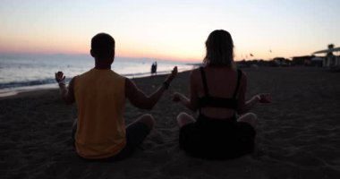 Akşamları kumsalda, alacakaranlıkta, yakın planda meditasyon yapan bir çift. Denizde rahatlama kavramı