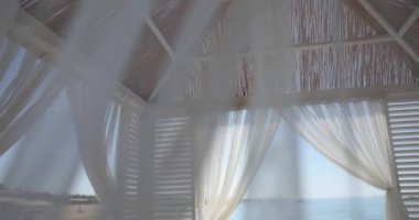 Beyaz şeffaf perdeleri olan bir deniz evi manzarası, yakın plan. Kumsalda dinlenmek için güzel bir bina.