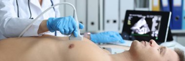 Klinikteki genç erkek hastaya kalp ultrasonu yapan doktor. Kalp patolojisi kavramının teşhisi ve tedavisi