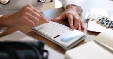 Steteskoplu bir doktor tıbbi hizmetlerin masraflarını ve gelirlerini hesaplar. Klinik hastanesinde hesap makinesi kullanan bir uygulayıcı