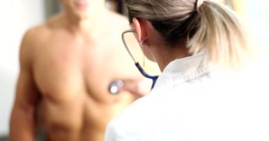 Doktor, steteskoplu genç bir sporcunun kalbini dinliyor. Yakın çekim 4K film ağır çekim. Kardiyovasküler hastalıkların teşhisi ve tedavisi