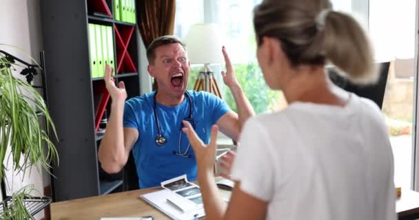 診療所で患者と一緒にいる若い男性医師は 女性患者に怒りの叫びに悩まされ フラストレーションを感じている 怒りの叫びと手を上げる医療 — ストック動画