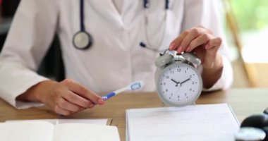 Dişçinin elinde çalar saat ve diş fırçası var. Ağız temizliği kavramı ve dişlerini fırçalama zamanı.