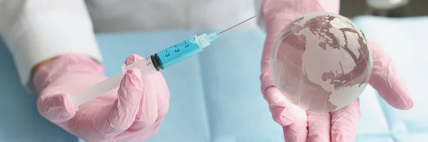 Close-up of medical worker hold syringe and miniature world globe in hands. Coronavirus injection, vaccination. Stop pandemic, shot, immunization concept