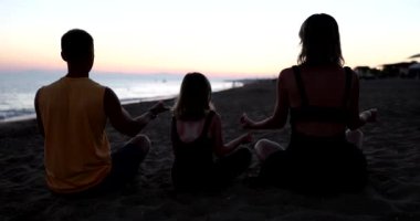 Aile, plajda yoga yaparken birlikte meditasyon yapar. Konsantrasyon ve sağlık ebeveynleri ve kızı birlikte spor yapıyor.