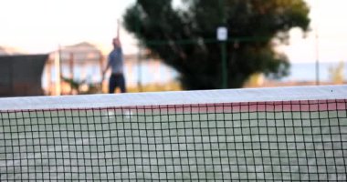 Tenis antrenmanındaki adam tenis kortunda topa vuruyor. Ağ aracılığıyla tenis antrenmanı