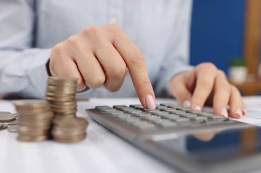 Ofisteki bir kadın madeni paraların yakınındaki hesap makinesine güvenir. Bir depozitonun faizi