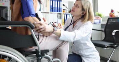 Doktor, tekerlekli sandalyedeki hamile kadının karnını steteskopla dinliyor. Hamilelik ve sakatlık kavramı