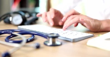 Doktor steteskop yakınındaki bilgisayar klavyesinde 4K 'lık filmi yavaş çekimde daktilo ediyor. Tıp eğitimi kavramı 