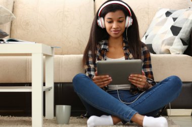 Uygulama yoluyla evde yabancı dili öğrenin. Kulaklıkta elinde tabletle oturan odaklanmış ırk kadını ve uzak bir kız öğrenci.