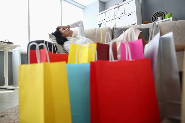 Tired woman sleeping on sofa with bags on floor. Shopping fatigue and stress