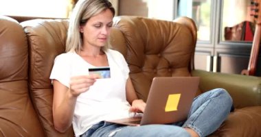 Kadın kanepede dizüstü bilgisayar kullanarak oturuyor ve kredi kartıyla alışveriş yapıyor. Kanepe ve iş konseptiyle online ödeme yapan kızı satın almak