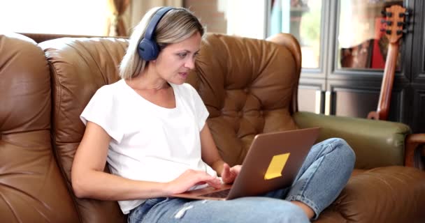 Een Vrouw Met Een Koptelefoon Bank Kijkt Naar Het Laptopscherm — Stockvideo