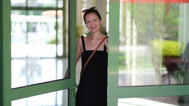 Gülümseyen genç bir kadın otel ve mağazanın ön kapısını açıyor. Hoş geldiniz ve misafirperverlik.