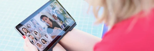 A woman by the pool holds a tablet on her lap, close-up, blurry. Girl video blogger saying hello to followers
