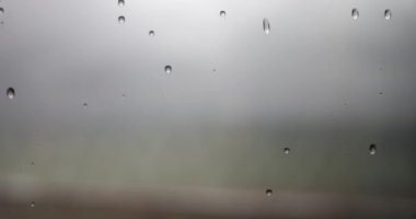 Penceredeki yağmur damlaları gri gökyüzüne yakın çekim yapıyor. Bulutlu ve kasvetli hava konsepti