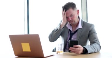 İş adamı ofiste alkol içer ve akıllı telefonlara bakar. Alkolizm ve işçi girişimcisi umutsuzluğa kapılmış bir adam iş yerinde oturuyor.