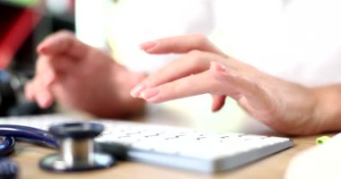 Kadın doktorun elleri bilgisayar klavyesinde çalışıyor ve hastaya uzaktan danışıyor. Klavyede yazan terapist ve kardiyolog tıbbi uygulamalar kullanıyor