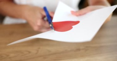 Kişi kalbini kağıttan keser ve makasla kart yapar. Sevgililer Günü konsepti ve uygulaması