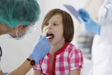 Klinikteki doktor küçük bir kızın boğazına bakıyor. Yakın plan, bulanık. Çocuk doktorunun çocuk muayenesi, teşhis