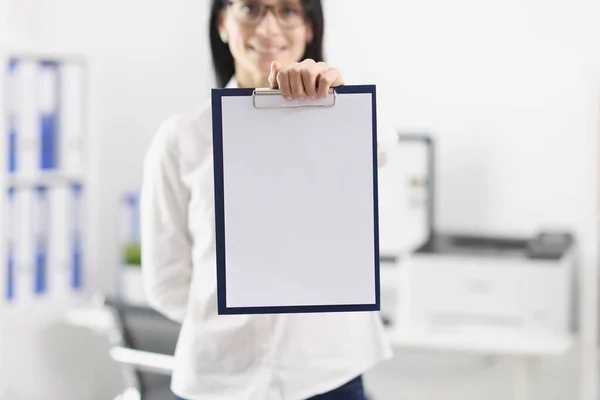 Woman in the office shows a folder with a blank document, mock up, close-up, blurry. Workspace, mentor businesswoman