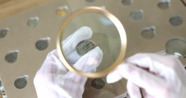 Numismatist, eski paraya büyüteçle bakıyor. Yakın çekim 4K film yavaş çekim. Hobi madeni para toplama kavramı 