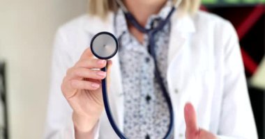 Kadın doktor ellerinin steteskop tutarak baş parmağını kaldırdığı yakın plan. Terapist kaliteli tıbbi bakım ve sigorta öneriyor.