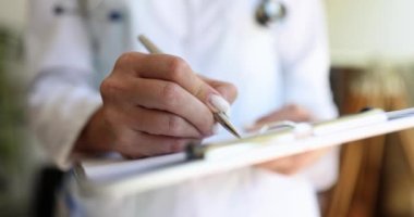 Dosyanın üzerine kalemle yazı yazan bir kadın doktorun yakın çekimi. Terapist danışmanlığı, klinik resepsiyon bölümü