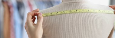 Bir mankenin üzerinde mezura ölçüsü olan bir terzinin elleri, yakın plan. Tasarım stüdyosu, moda evi