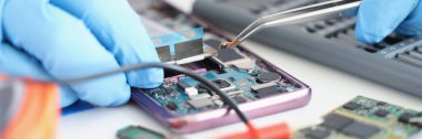 Eller cımbızla akıllı telefon mikroçipi tutuyor, yakın plan, bulanık. Telefon güncelleme ve onarım, atölye