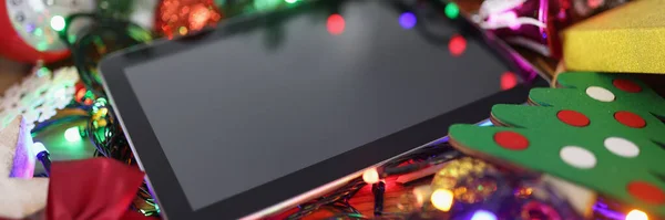 Close-up of tablet with black screen, turned off device on christmas decoration, mockup. Watch festive show on new year, decor your home with colourful lights. Christmas, technology concept