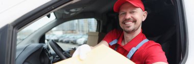 Kırmızı üniformalı bir kurye, arabada oturuyor ve bir paket tutuyor, yakın plan. Kargo, dağıtım, temsilci