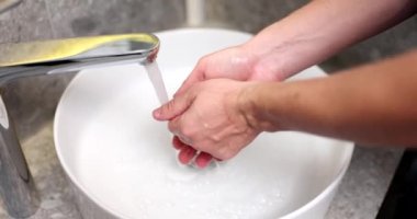 Adam dokunmadan musluktan ellerini yıkıyor. Yakından. El hijyeni kavramı