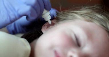 Kulak zarı iltihabı olan çocuğa kulak arkası 4K film yavaş çekimde antibiyotik veriliyor. Çocuk konseptinde kulak hastalıklarının tedavisi