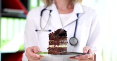 Doktor diyetisyen elinde çikolatalı pasta tutuyor. 4K 'lık filmi yavaş çekimde. Abur cubur aşırı karbonhidrat konsepti